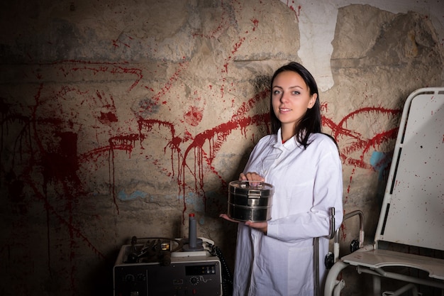 血が飛び散った壁の前にアルミの箱を持っている女性科学者、ハロウィーンのコンセプト