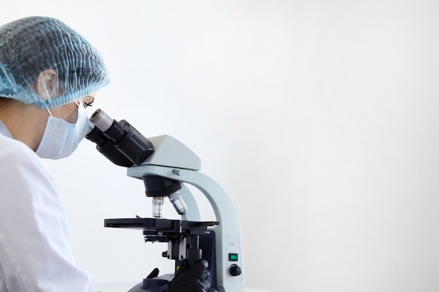 Female scientist looking through microscope in modern chemical laboratory doing some research