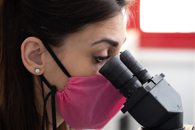 Female scientist sitting at microscope gazing into eyepieces