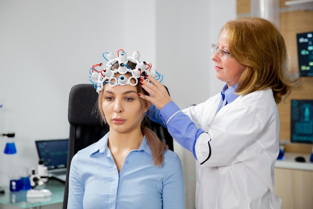 Foto scienziata che mette il casco per la scansione delle onde cerebrali su una paziente. dispositivo moderno e tecnologia