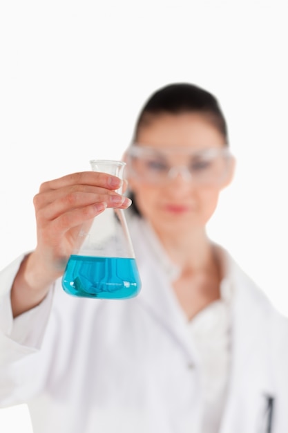 Female scientist with safety glasses holding a blue flask