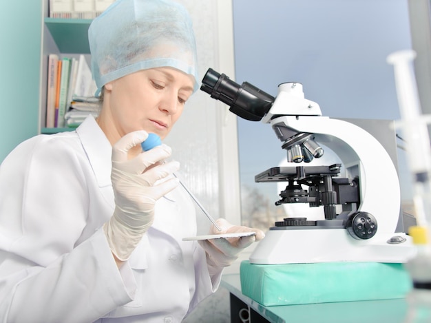 Female scientist working at the laboratory. White uniform and gloves. Focus on the face and hands.