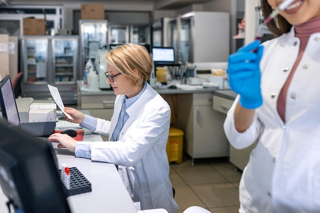 Female Scientists Working on their Computers In Big Modern Laboratory Various Shelves with Beakers Chemicals and Different Technical Equipment is Visible