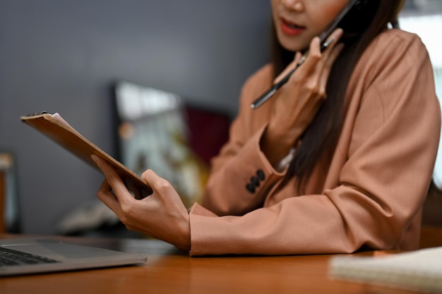 Photo female secretary looking the details on paper while talking on the phone cropped image