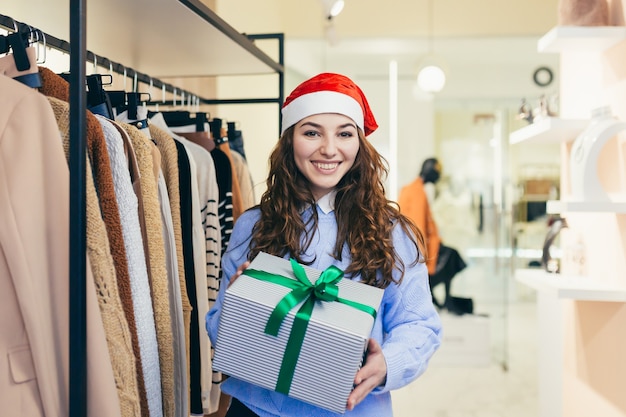 女性の売り手はクリスマスの服で衣料品店にクリスマスプレゼントを提供します