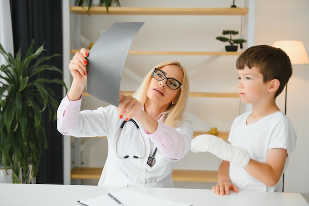 Pediatra senior femminile che mostra i raggi x del polso e della mano al paziente del ragazzino bambino presso l'ufficio del medico