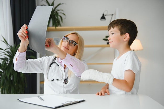 Pediatra senior femminile che mostra i raggi x del polso e della mano al paziente del ragazzino bambino presso l'ufficio del medico