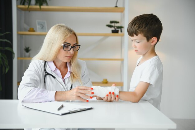 Pediatra senior femminile che mostra i raggi x del polso e della mano al paziente del ragazzino bambino presso l'ufficio del medico