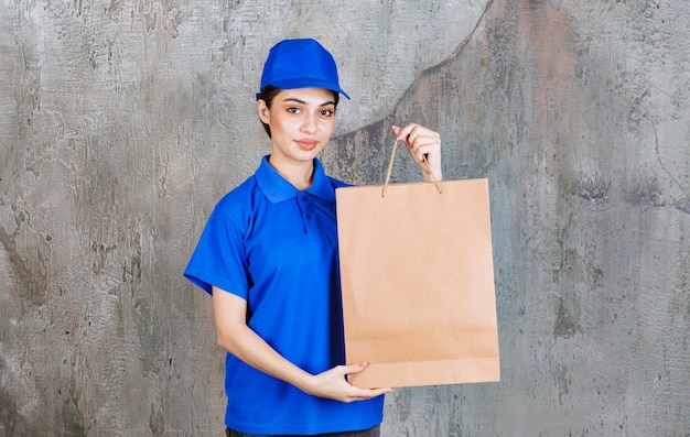 Female service agent in blue uniform holding a cardboard shopping bag.