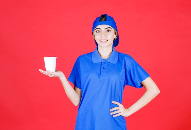 Female service agent in blue uniform holding a disposable cup of drink . 