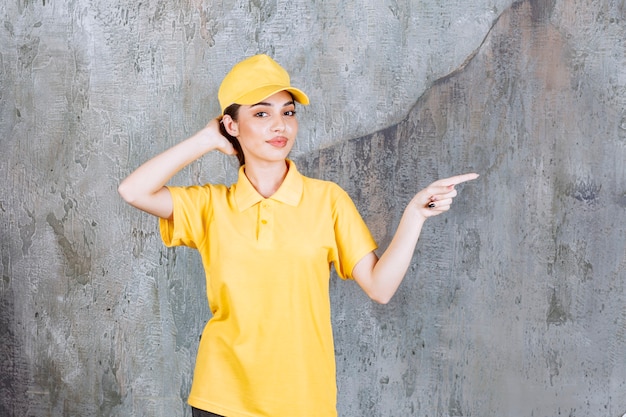 Female service agent in yellow uniform standing on concrete wall and pointing to the right side.