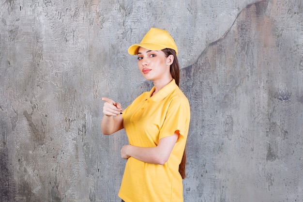 Agente di servizio femminile in uniforme gialla in piedi sul muro di cemento e mostrando la persona davanti.