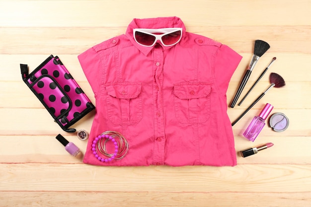 Female shirt and cosmetics on wooden table top view