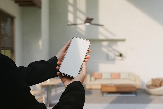 female showing a smartphone screen mockup over blurred modern comfortable living room