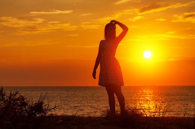 ビーチで夕暮れ時の女性のシルエット、手を挙げろ