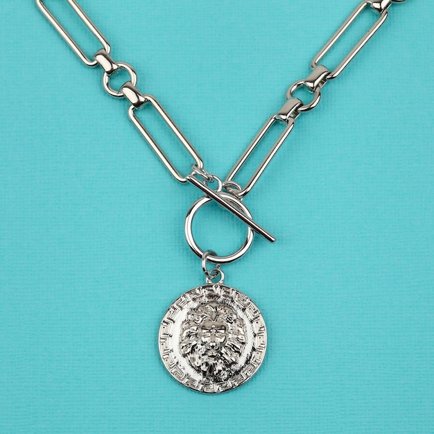 Female silver lion head pendant with chain on bright blue textured background Closeup shot