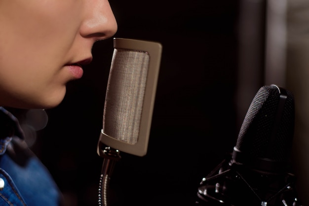 Female singer mouth singing on microphone, on black