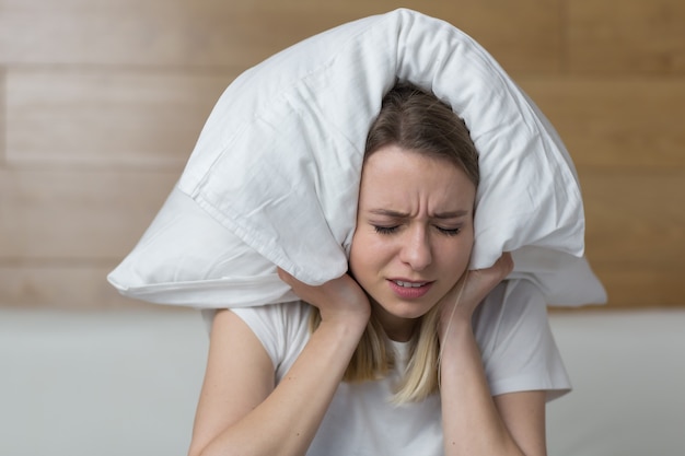 female sit on couch cover ears with hands annoyed by noisy 