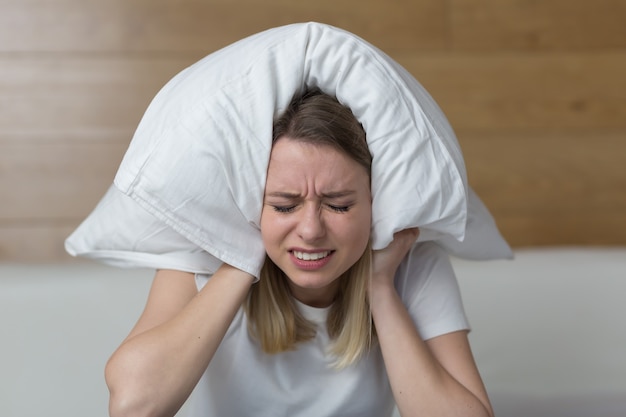 female sit on couch cover ears with hands annoyed by noisy 