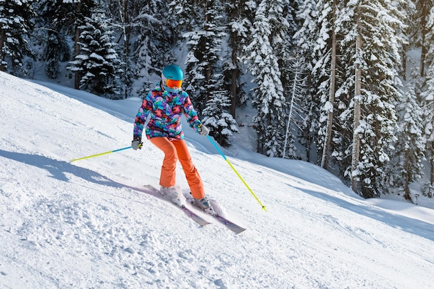 Female skier in bright clothes sliding down the slope on a sunny day at a mountain resort