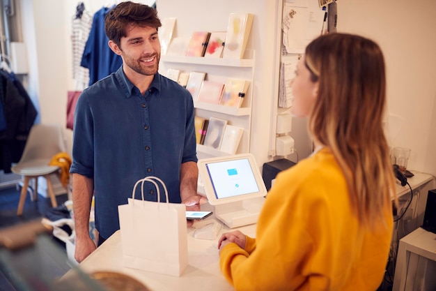 Foto proprietario di una piccola impresa femminile che accetta pagamenti contactless in negozio dal cliente tramite telefono cellulare