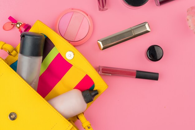 Female small handbag full of cosmetic products on bright pink background