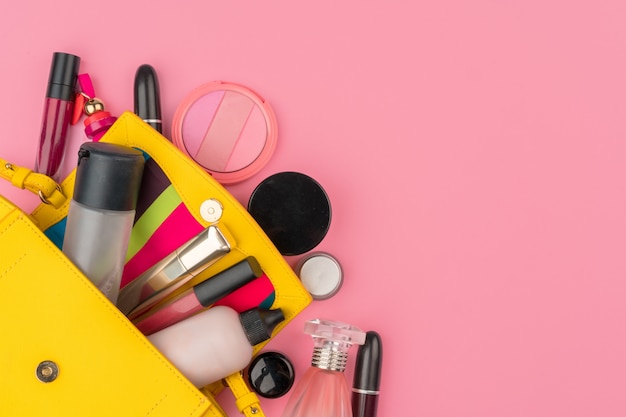 Female small handbag full of cosmetic products on bright pink background