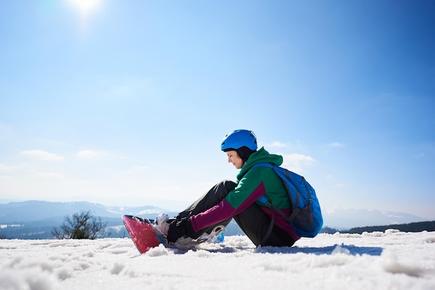 Female snowboarder adjusting snowboard ion copy space background of blue sky and winter mountains