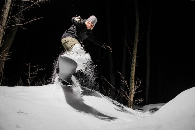 Female snowboarder riding down the mountain slope at night