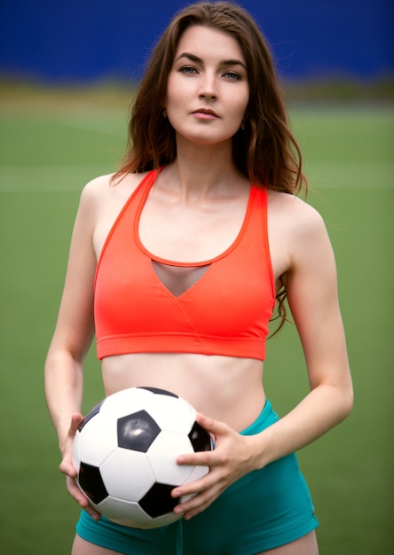 A female soccer player in a top and shorts holds a ball in her hands