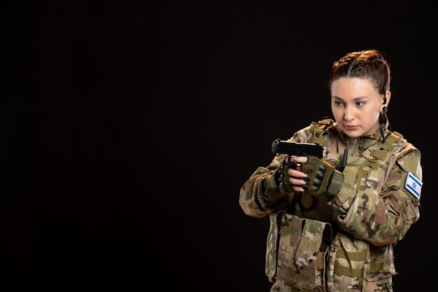 Female soldier in camouflage holding gun on black wall
