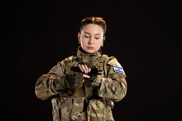 Female soldier in camouflage reloading gun on black wall