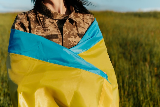 Soldato femminile vestito in uniforme militare avvolta nella bandiera ucraina