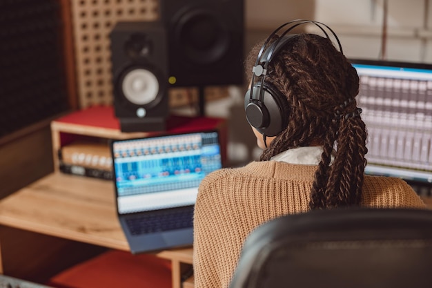 Female sound engineer musician with headphones sitting at desk with laptop while recording new song