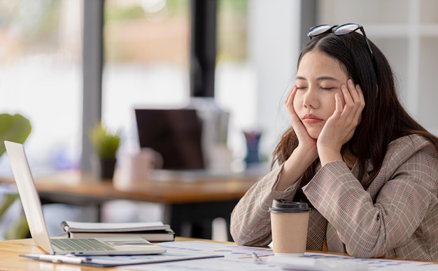 女性のスタートアップ従業員は、彼女が疲れていて、オフィス症候群を持っていることを強調している会社で会計と財務の仕事をしている彼女が一日中働くことからストレスを感じているように見えますハードワークの概念