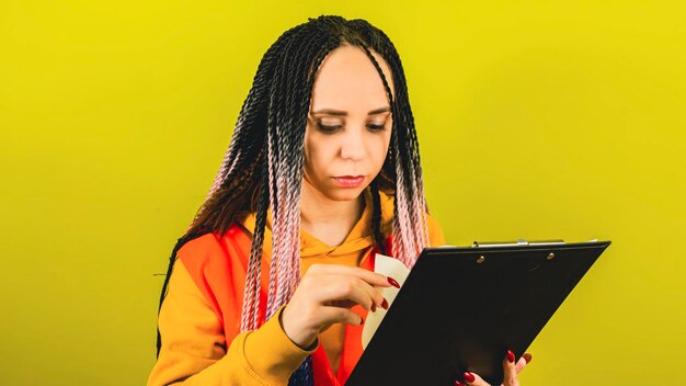 Female storekeeper in orange vest with clipboard young woman with working document on yellow background in studio