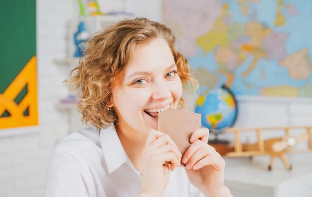 Female student closeup portrait young teacher or tutor eat\
chocolate at classroom in school woman education