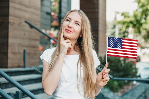 写真 女子学生は、大学の建物を背景に小さなアメリカの国旗を考え、夢を見て、持っています