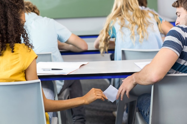 Female student passing note to friend in classroom