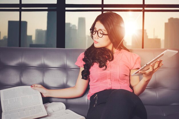 Female student reads book and use tablet on couch