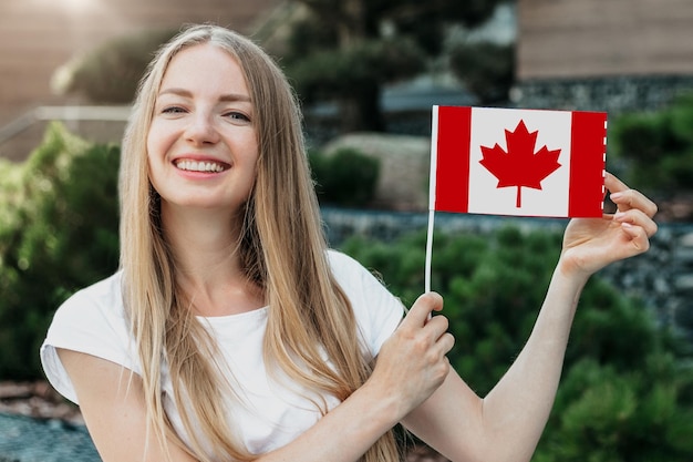 Female student shows a small canadian flag and stands against the background of the university and smiling