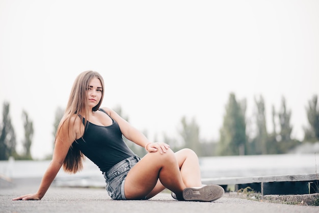 A female student sits crosslegged on the road in summer and looks at the camera natural background