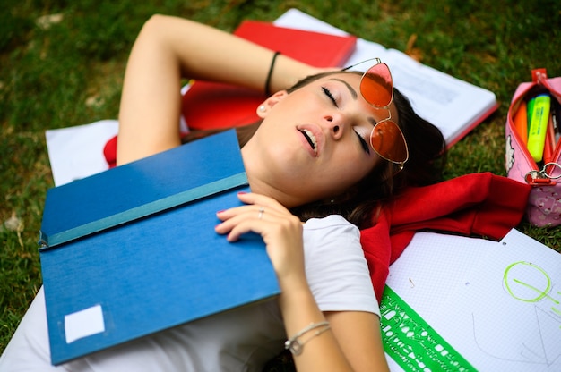 Female student sleeping on the grass with a book covering her