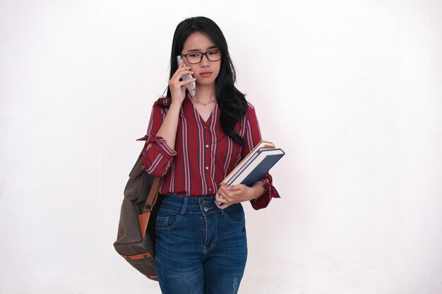 Female student standing and making a phone call while carrying some books and a school bag