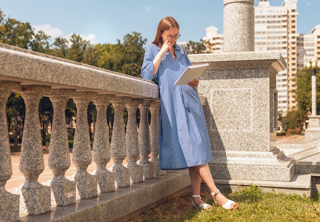 Female student standing near university and reading book preparing for exam