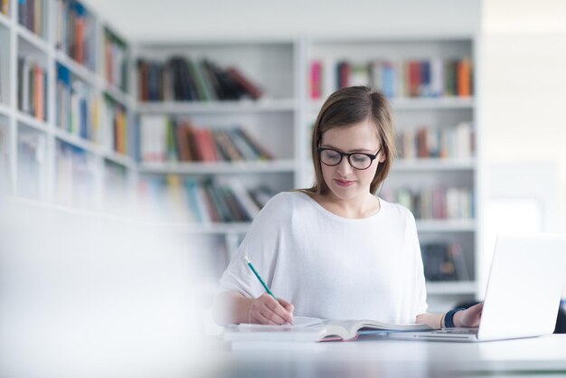 女子生徒が学校の図書館でラップトップを使って勉強しインターネットで情報を探しています