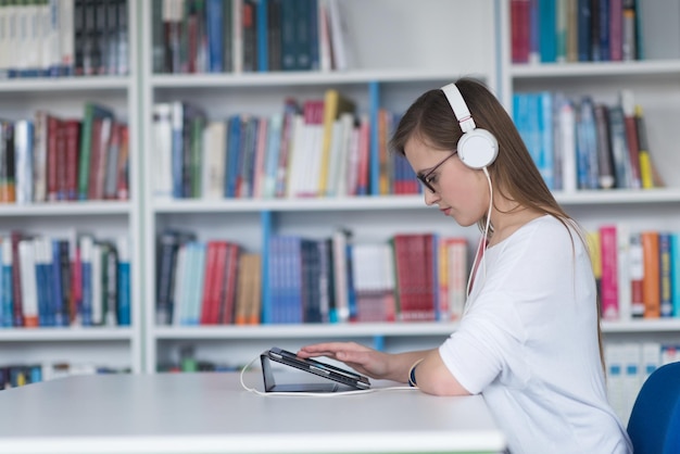 female student study in school library using tablet and searching for information's on internet Listening music and lessons on white headphones