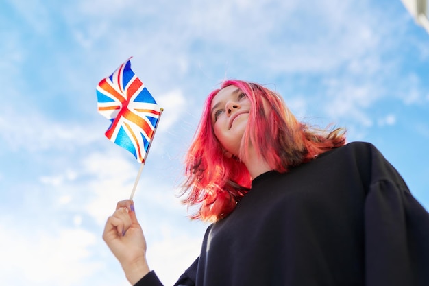 写真 雲の背景と英国の旗の青い空を持つ女子学生ティーンエイジャー英国王国イングランド教育と若者の愛国心の人々の概念