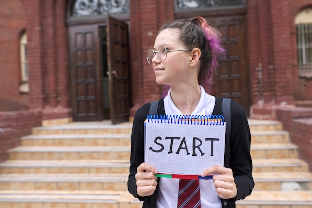 メモ帳と手書きの単語の開始、校舎の背景を持つ女子学生のティーンエイジャー。学校に戻る、大学教育の概念に戻る