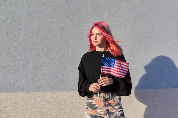 Female student teenager with usa flag in hand gray outdoor wall\
background united states of america education and youth patriotism\
people concept